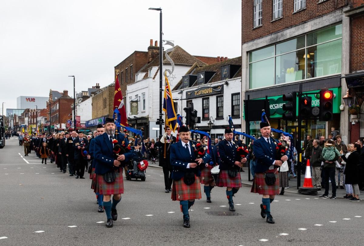 A parade of military musicians walking through Eltham High Street playing bag pipes