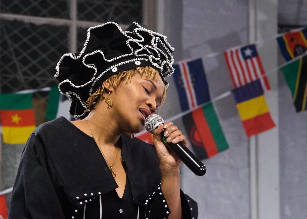 A woman singing into a microphone with flags of different African nations behind her.