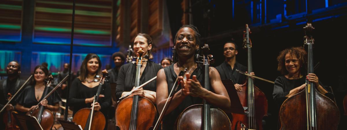 A group of musicians, each holding a string instrument and clapping