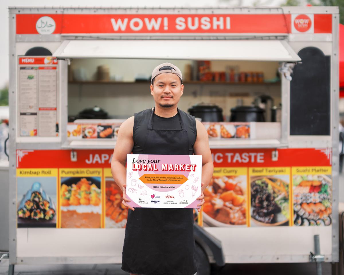 A market trader proudly standing in front of his food truck.