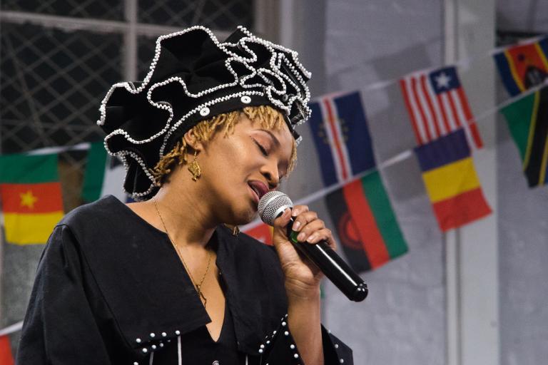 A woman singing into a microphone with flags of different African nations behind her.