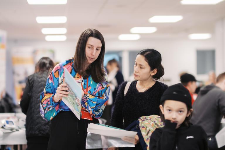 a mother standing with her son being shown a leaflet by a member of staff