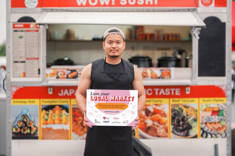 A market trader proudly standing in front of his food truck.