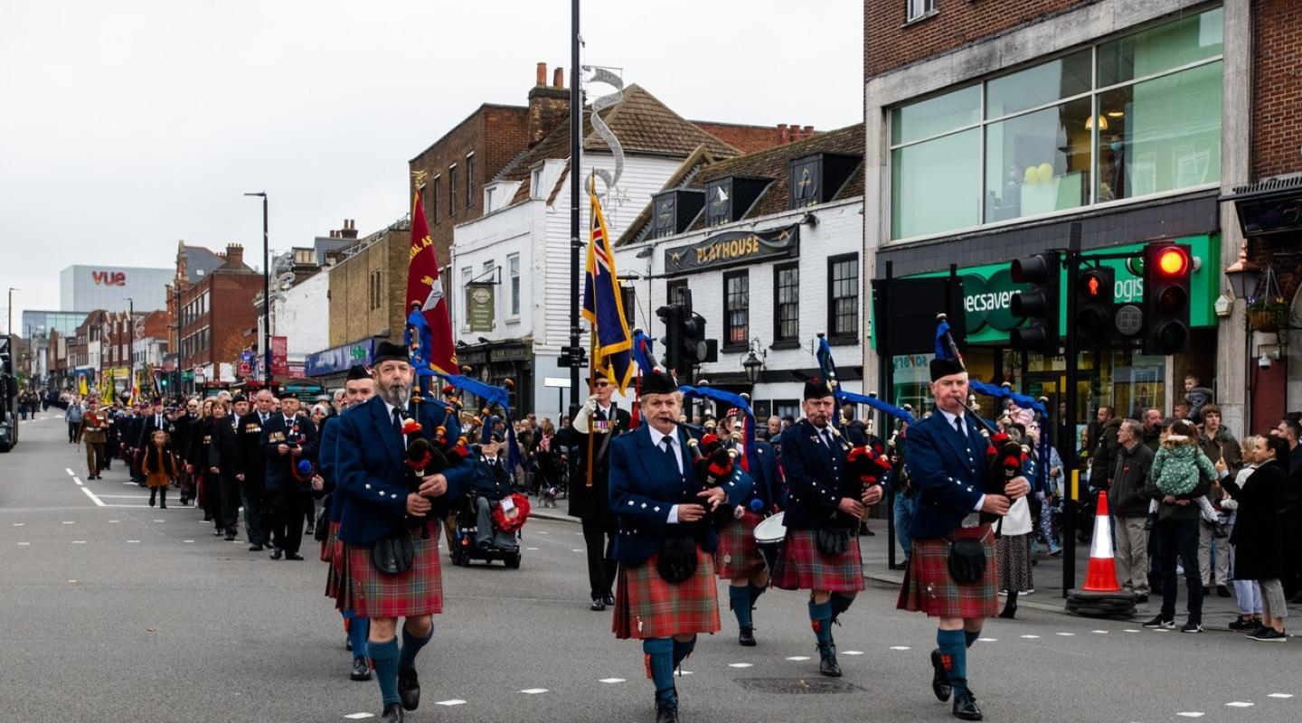 A parade of military musicians walking through Eltham High Street playing bag pipes